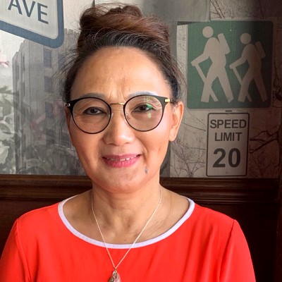 Sunny smiles at the camera. She is an Asian woman in her 60s, wearing a red shirt.